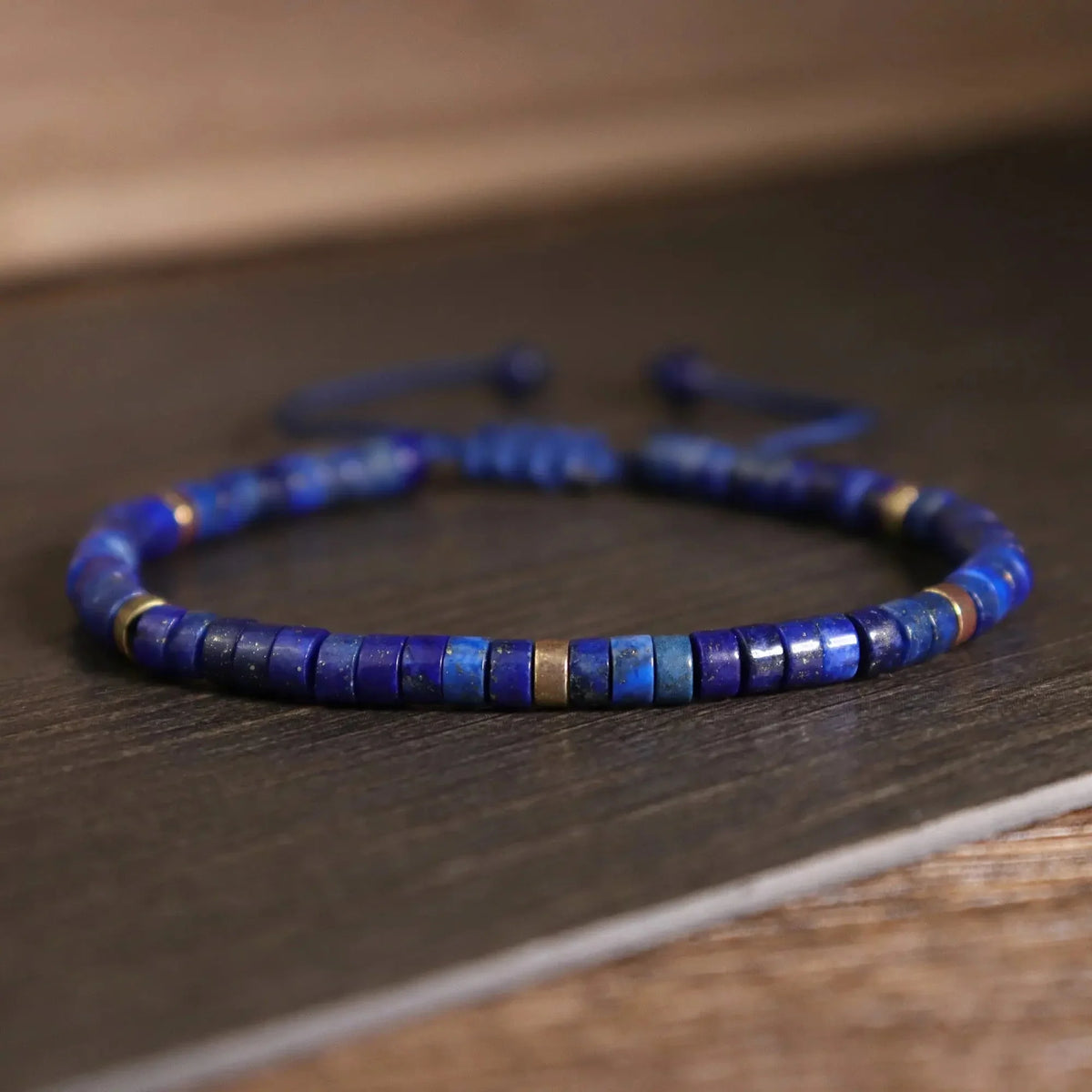 Slim blue cylindrical bead bracelet on a dark wooden surface
