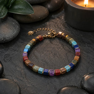 7 chakra bracelet with golden hematite on dark slate beside a candle, styled meditation flat lay