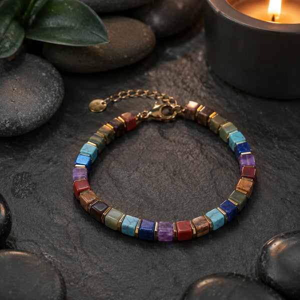 7 chakra bracelet with golden hematite on dark slate beside a candle, styled meditation flat lay