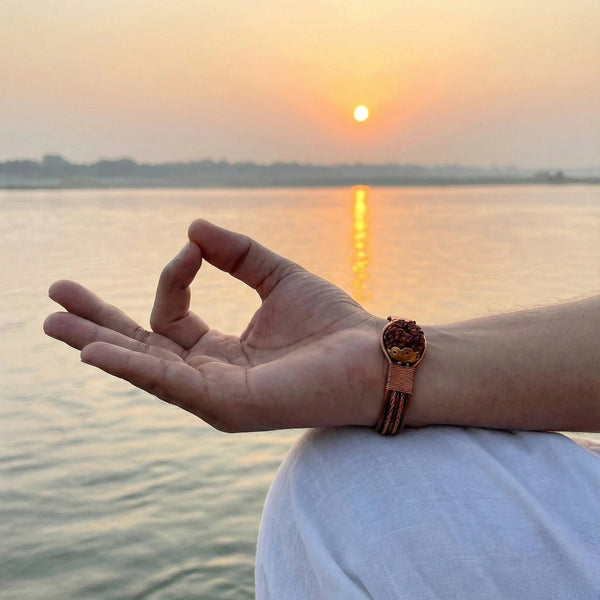 Nepali copper rudraksha bracelet worn on wrist in meditation mudra by a river at sunset