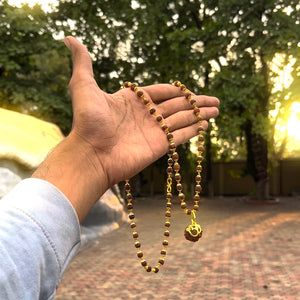 Gold-plated rudraksha Om Shree mala held in hand outdoors at golden hour, showing full necklace length