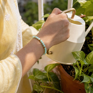 Woman wearing the Amazonite bracelet, watering a balcony plant
