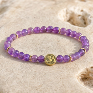 Close-up of the Amethyst 4mm Bracelet with Om Charm on a pale stone surface
