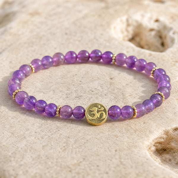 Close-up of the Amethyst 4mm Bracelet with Om Charm on a pale stone surface