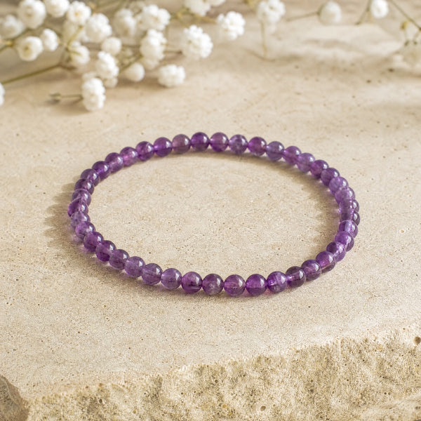 Soultheory Amethyst 4mm Round Bead Bracelet on a sandstone block with white flowers