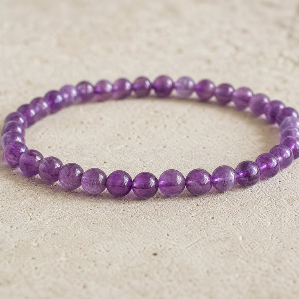 Close-up of the Amethyst 4mm Round Bead Bracelet on a pale stone surface