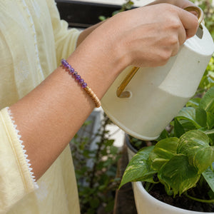 Woman wearing the Amethyst bracelet, watering a balcony plant