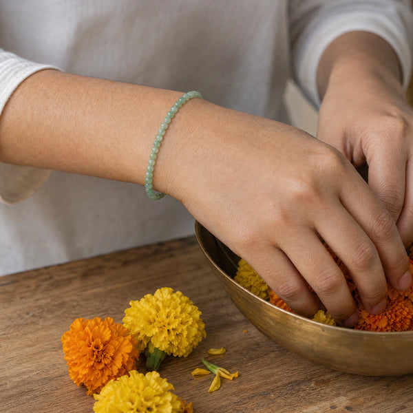 Woman wearing the Aventurine bracelet, arranging marigold flowers