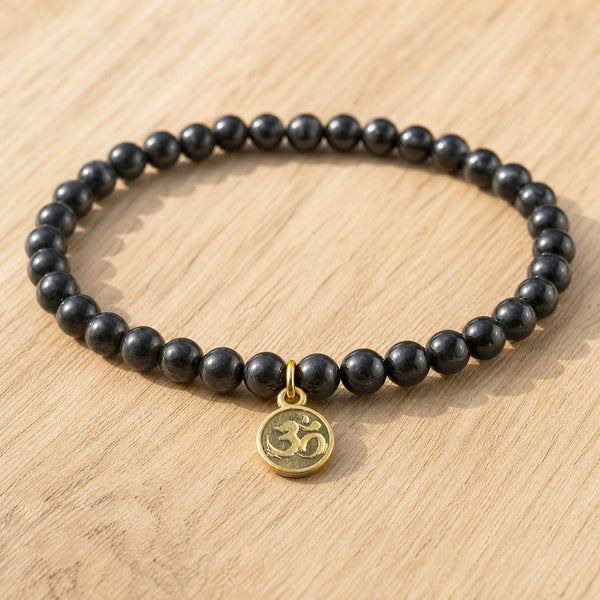 Close-up of the Black Tourmaline 4mm Bracelet with Om Charm on a light oak board