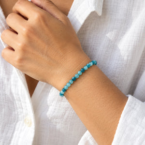 Woman wearing the Blue Apatite 4mm Round Bead Bracelet with a white linen shirt