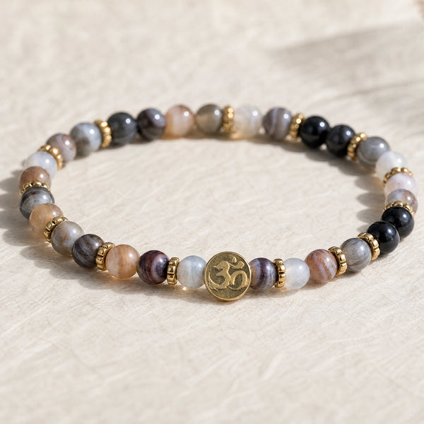 Close-up of the Botswana Agate 4mm Bracelet with Om Charm on cream handmade paper