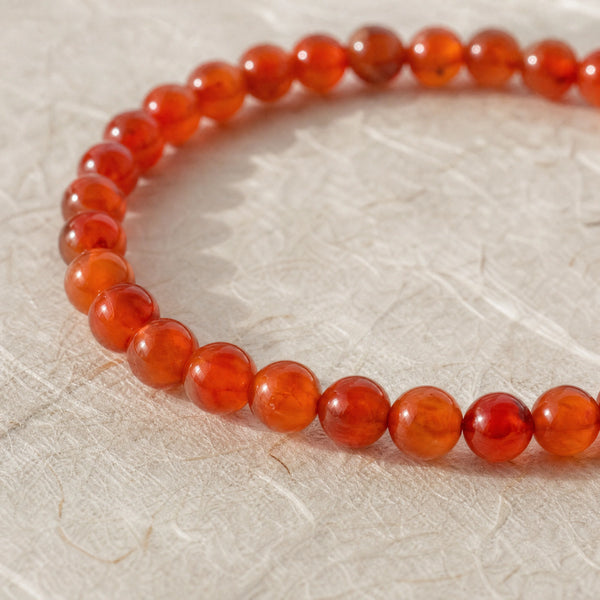 Close-up of the Carnelian 4mm Round Bead Bracelet on cream handmade paper