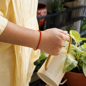 Woman wearing the Carnelian bracelet, watering a balcony plant