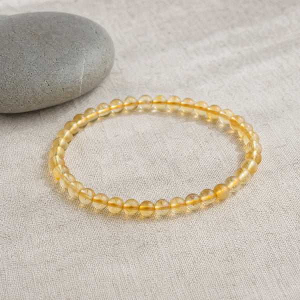 Soultheory Citrine 4mm Round Bead Bracelet on beige linen beside a river pebble