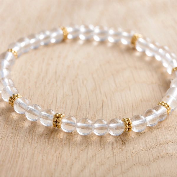 Close-up of the Clear Quartz 4mm Bead Bracelet with Gold Spacers on a light oak board
