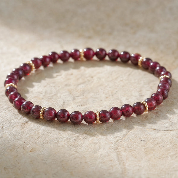 Close-up of the Garnet 4mm Bead Bracelet with Gold Spacers on a pale stone surface