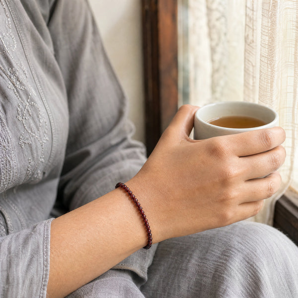 Woman wearing the Garnet bracelet, holding a mug of tea