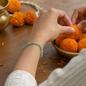 Woman wearing the Green Aventurine bracelet, arranging marigold flowers