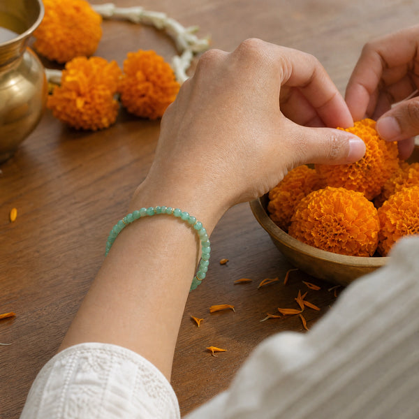 Woman wearing the Green Aventurine bracelet, arranging marigold flowers