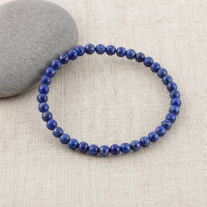 Soultheory Lapis Lazuli 4mm Round Bead Bracelet on beige linen beside a river pebble