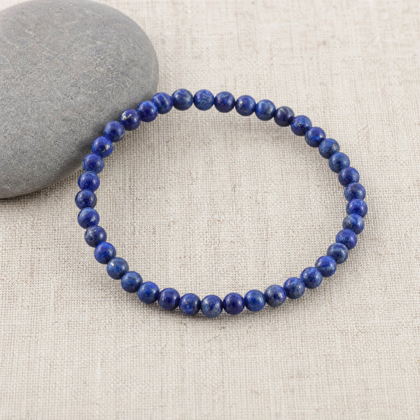 Soultheory Lapis Lazuli 4mm Round Bead Bracelet on beige linen beside a river pebble