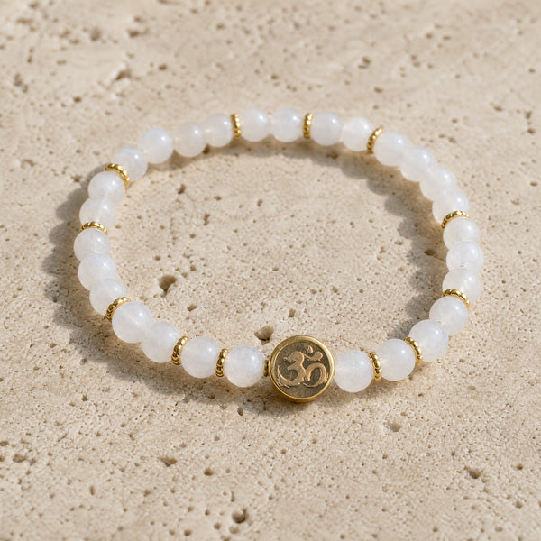 Close-up of the Moonstone 4mm Bracelet with Om Charm on pale travertine