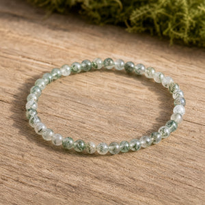 Soultheory Moss Agate 4mm Round Bead Bracelet on weathered oak beside moss