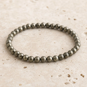 Close-up of the Pyrite 4mm Round Bead Bracelet on pale travertine