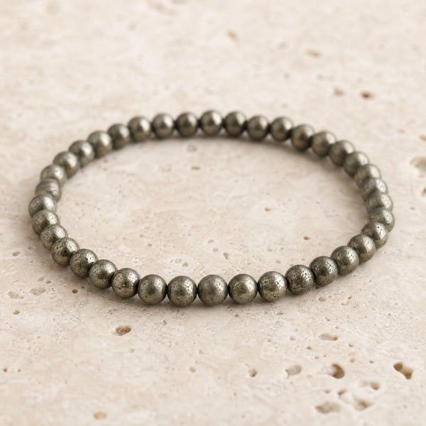 Close-up of the Pyrite 4mm Round Bead Bracelet on pale travertine