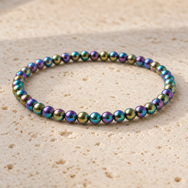 Close-up of the Rainbow Hematite 4mm Bead Bracelet on pale travertine
