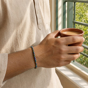 Man wearing the Rainbow Hematite bracelet, holding a cup of chai