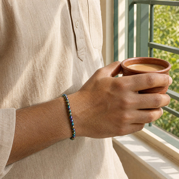 Man wearing the Rainbow Hematite bracelet, holding a cup of chai