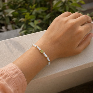 Woman wearing the Rainbow Moonstone 4mm Bracelet with Om Charm with a peach cotton top