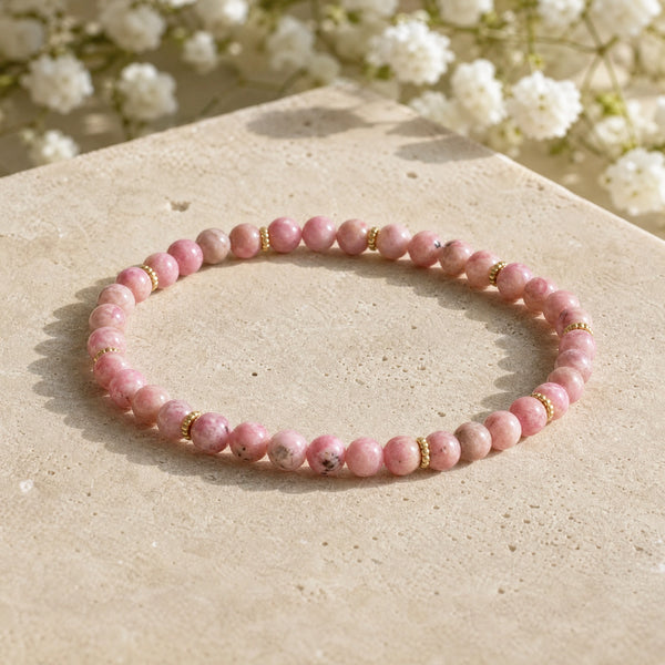 Soultheory Rhodonite 4mm Bead Bracelet with Gold Spacers on a sandstone block with white flowers