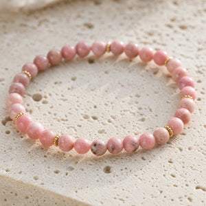 Close-up of the Rhodonite 4mm Bead Bracelet with Gold Spacers on a pale stone surface