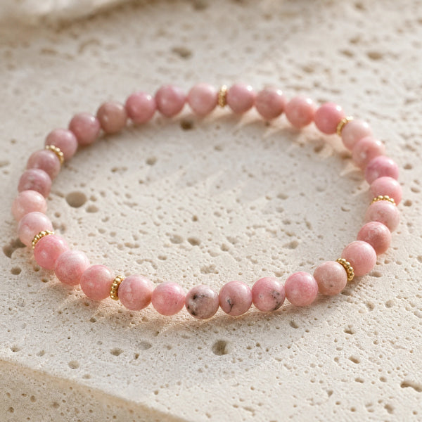 Close-up of the Rhodonite 4mm Bead Bracelet with Gold Spacers on a pale stone surface