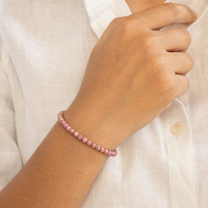 Woman wearing the Rhodonite 4mm Round Bead Bracelet with a white linen shirt