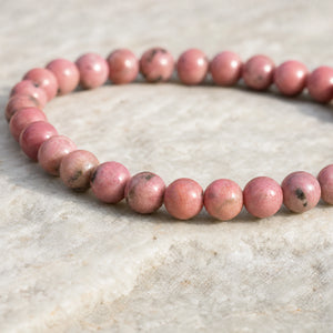 Close-up of the Rhodonite 4mm Round Bead Bracelet on a pale stone surface