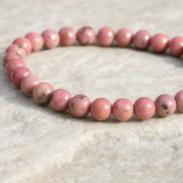 Close-up of the Rhodonite 4mm Round Bead Bracelet on a pale stone surface
