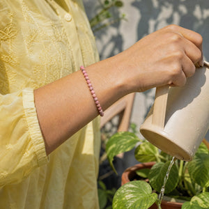 Woman wearing the Rhodonite bracelet, watering a balcony plant