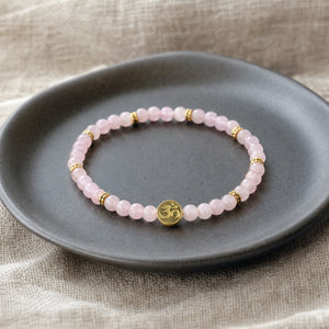 Soultheory Rose Quartz 4mm Bracelet with Om Charm on a charcoal ceramic dish on linen