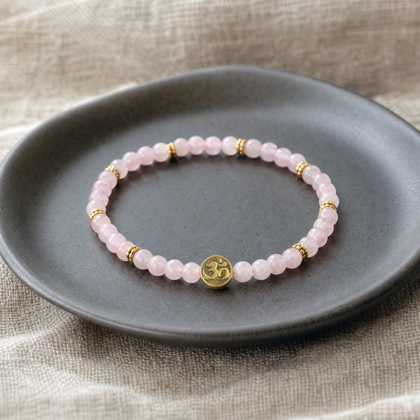 Soultheory Rose Quartz 4mm Bracelet with Om Charm on a charcoal ceramic dish on linen