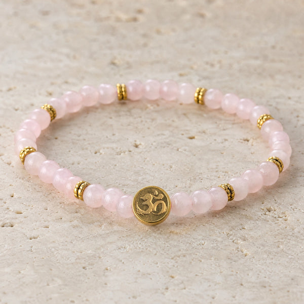 Close-up of the Rose Quartz 4mm Bracelet with Om Charm on pale travertine
