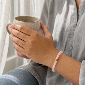 Woman wearing the Rose Quartz bracelet, holding a mug of tea