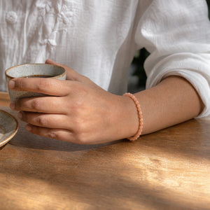 Woman wearing the Sunstone bracelet, holding a ceramic coffee cup