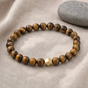Soultheory Tiger Eye 6mm Bead Bracelet with Gold Accent on beige linen beside a river pebble