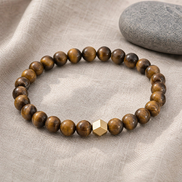 Soultheory Tiger Eye 6mm Bead Bracelet with Gold Accent on beige linen beside a river pebble