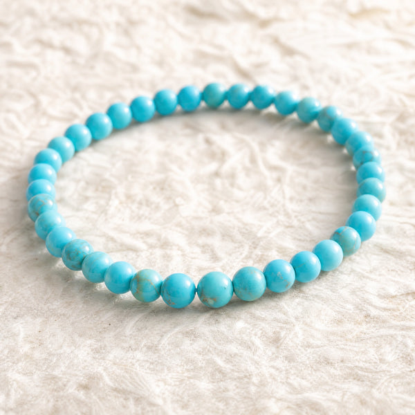 Close-up of the Turquoise 4mm Round Bead Bracelet on cream handmade paper