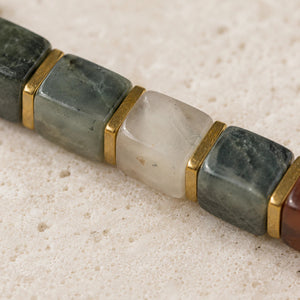 Close-up of green-and-red African bloodstone cube beads with gold spacers on travertine stone