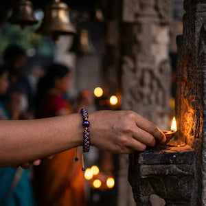 Amethyst cosmic eclipse bracelet on a wrist lighting a diya at a temple, cord wrapped beads